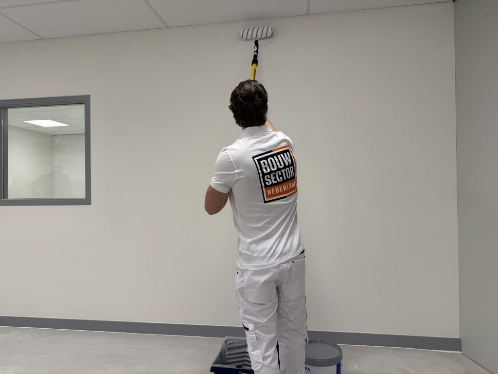 Schilder in wit werkshirt saust een lichte muur tot aan het plafond
