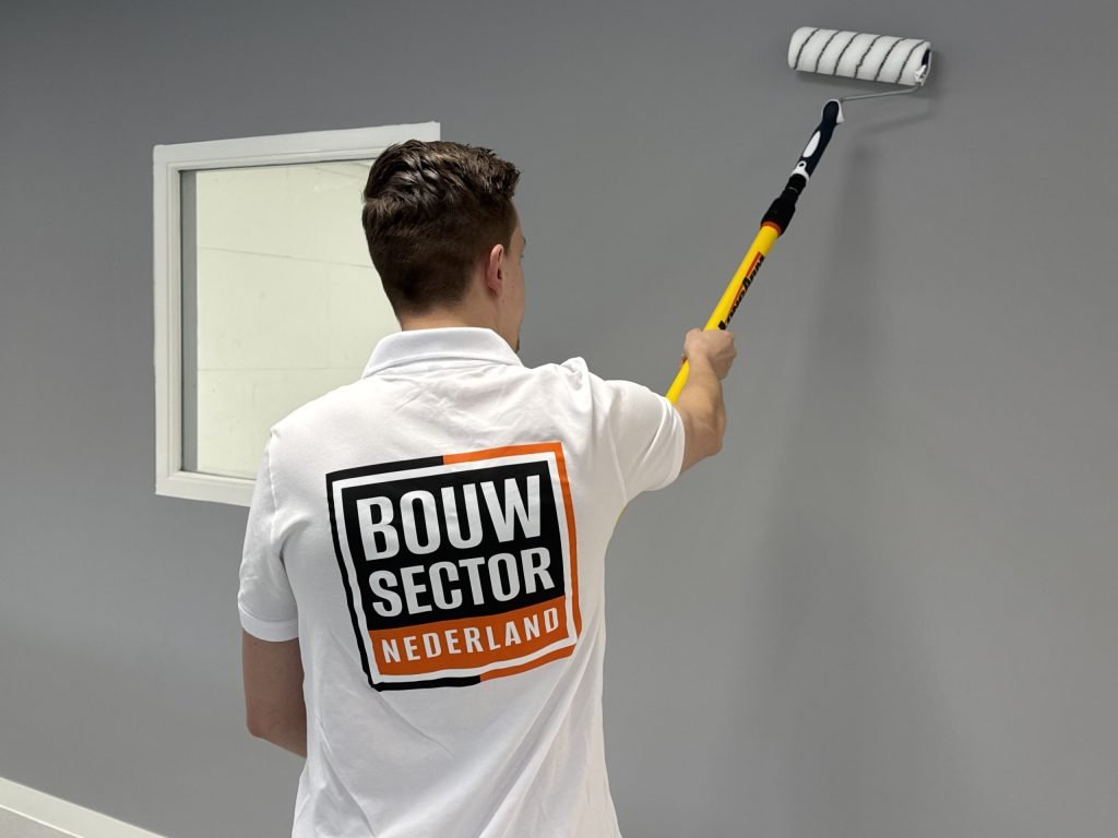 Schilder rolt een grijze laag muurverf bovenaan de wand naast een wit binnenraam