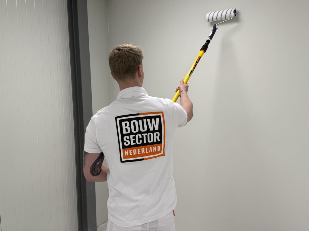 Schilder van Bouwsector Nederland rolt verf op een lichte muur in een smalle ruimte